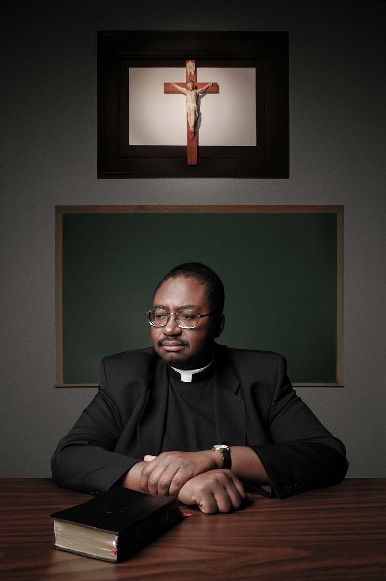 Father Raymond Lee Harris seated at a table with a bible in front of a crucifix at Mount St. Mary