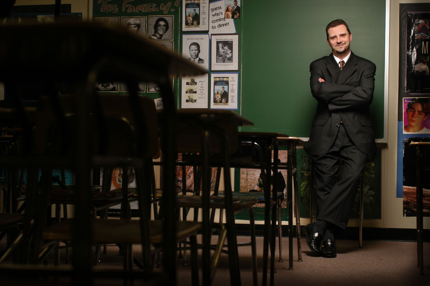 An elementary school teacher leans against a blackboard in his classroom