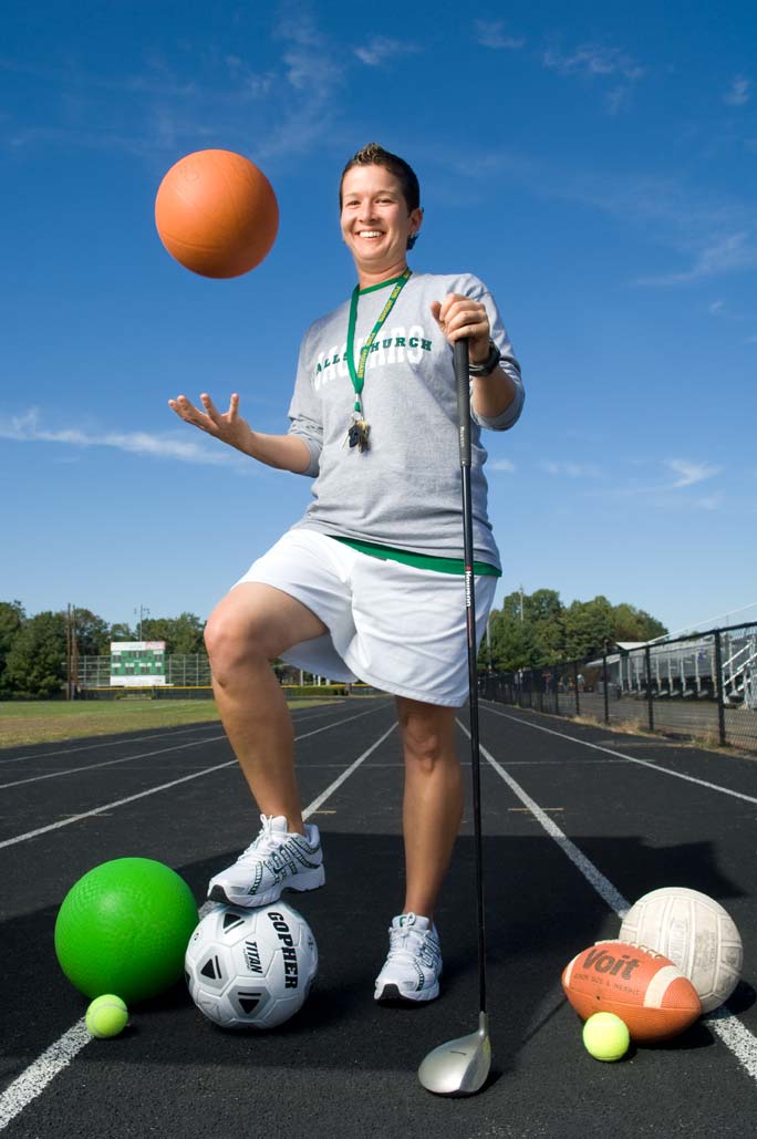 PE Teacher Heather Woodson stands on a high school track with an assortment of sports equipment