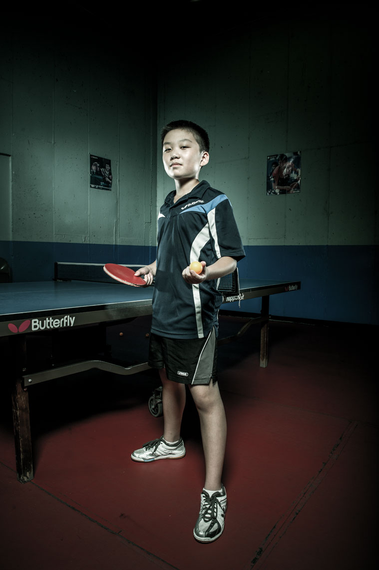 Table tennis player standing in front a of table holding a paddle with dramatic lighting