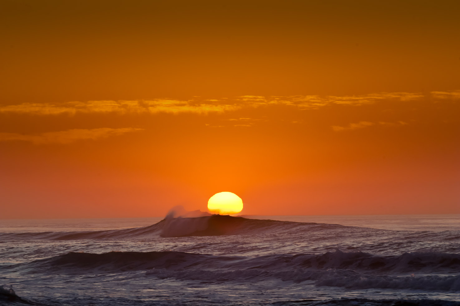 The sun sets behind a wave and seaspray at Asilomar State Beach, Pacific Grove, California