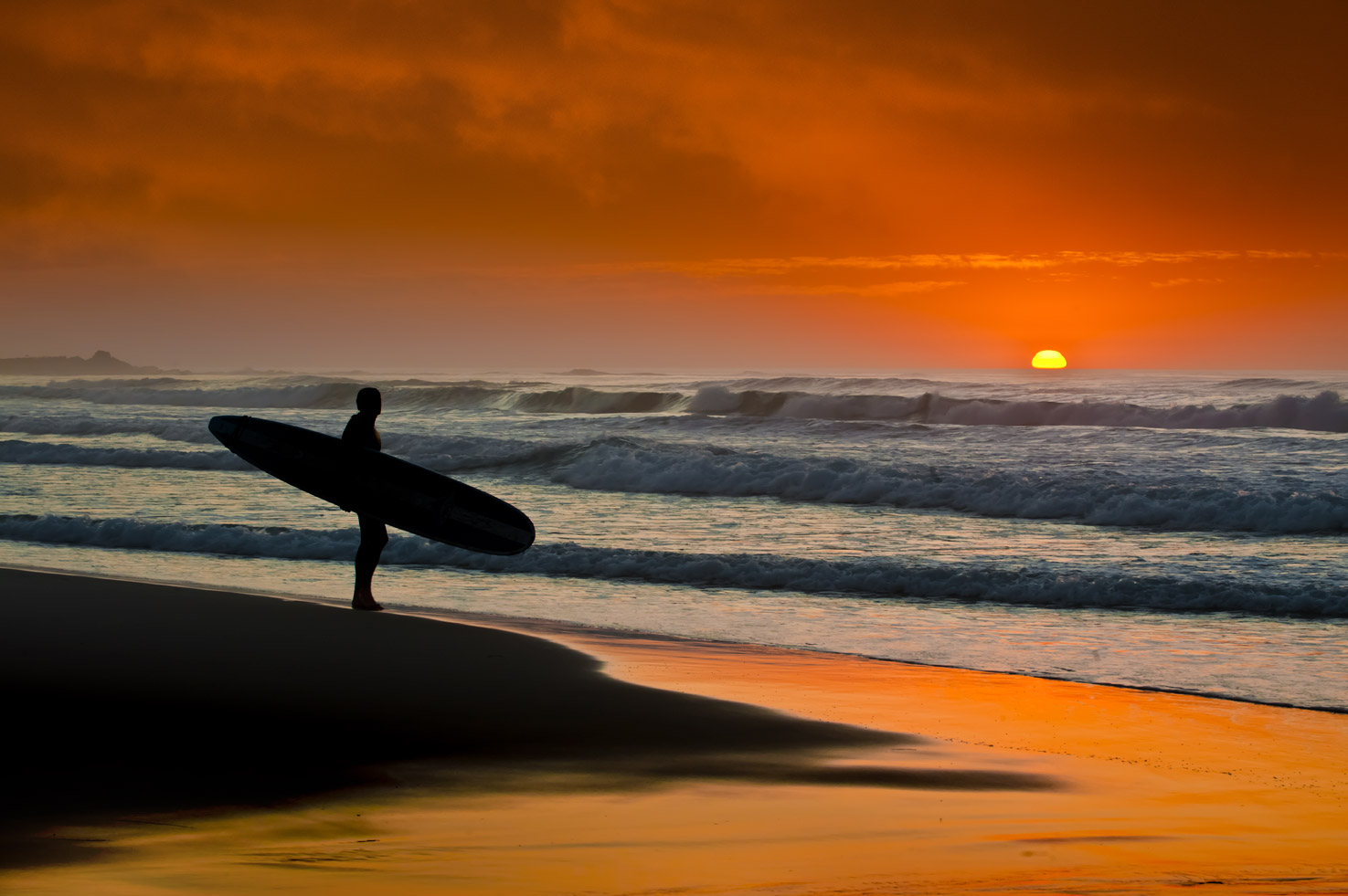 A surfer stands and watches the sunset at Asilomar State Beach, Pacific Grove, California