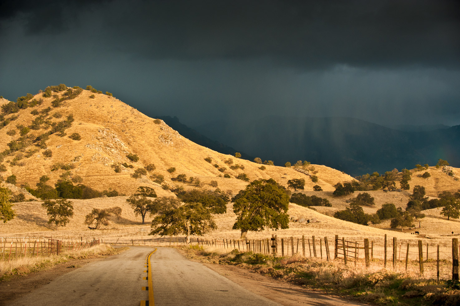 Rain falls in the distance as sun lights hills and a lonely road in the foreground in California