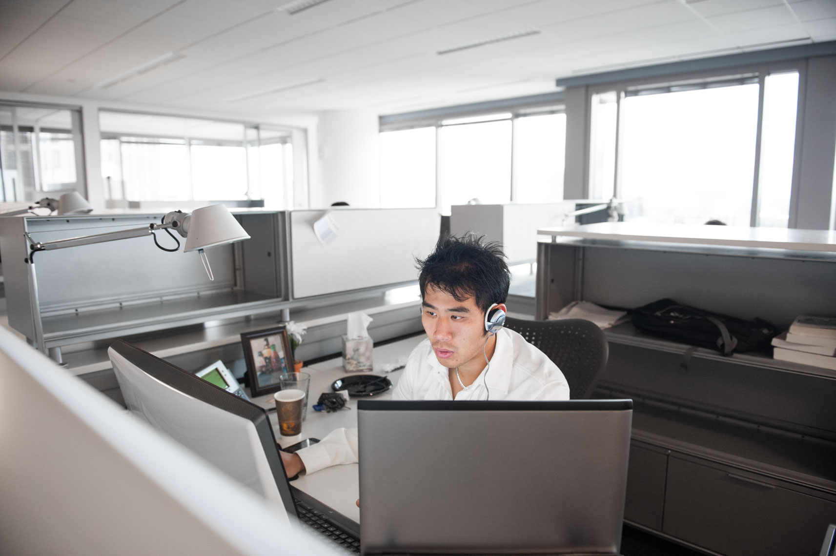 A man wearing an earpiece sits at a cubicle in an office space