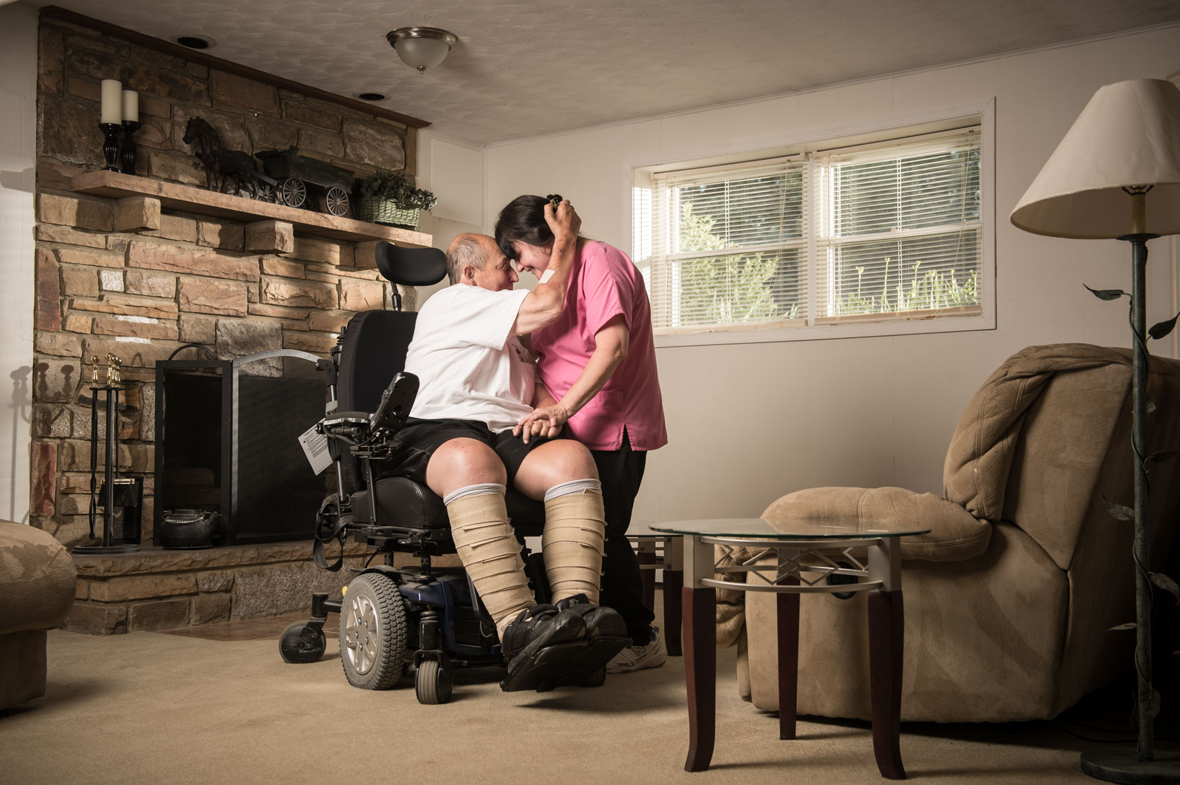ALS patient seated in his wheelchair holding hands with his nurse in a living room