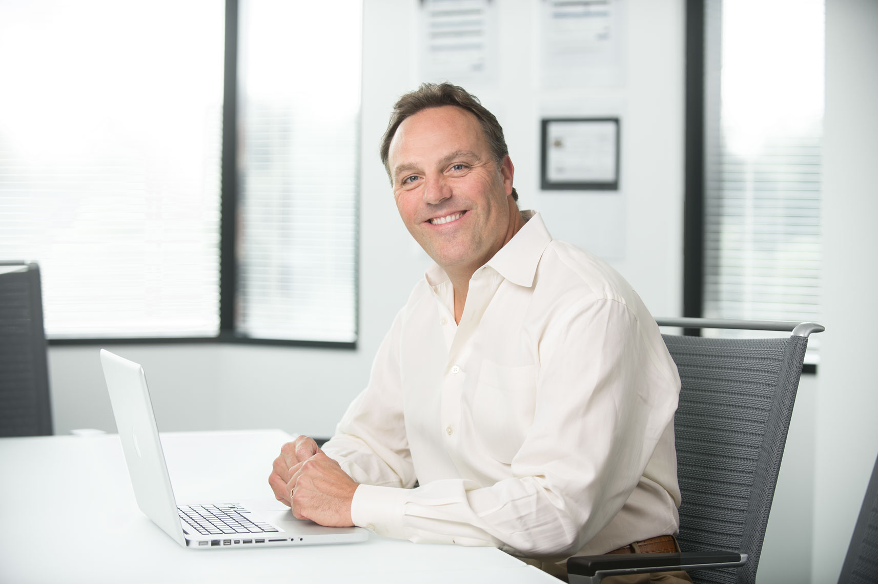 A man smiling with a laptop at a board room conference table