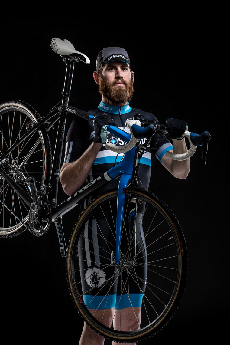 Team Crosshairs Cyclist Kevin Hays holding his bike on his shoulders in front of a black background