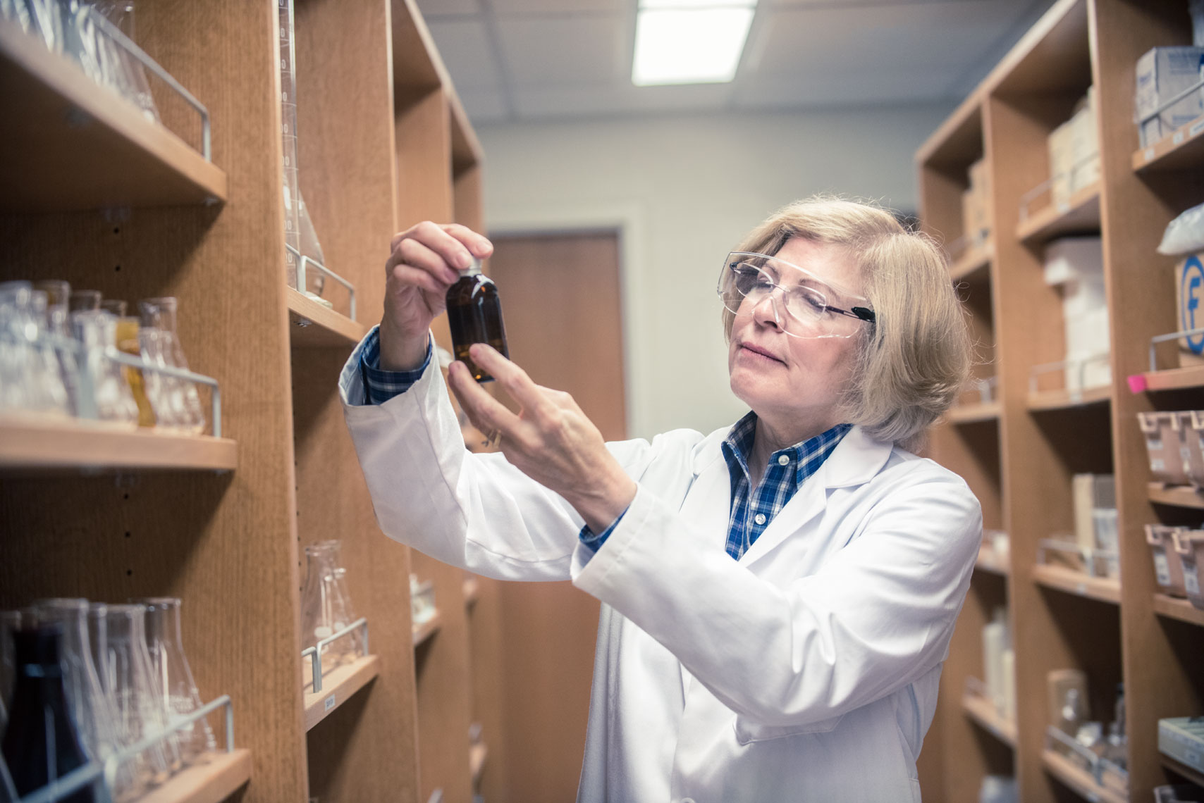 A pharmacist inspects a bottle in between shelves