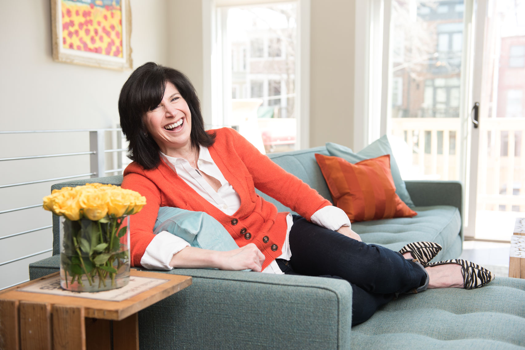 Woman in an orange sweater laughing on a couch