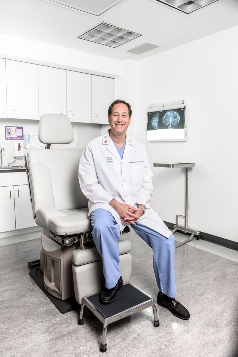 Dr. Neil Friedman wearing a lab coat and seated on an exam chair in a doctor