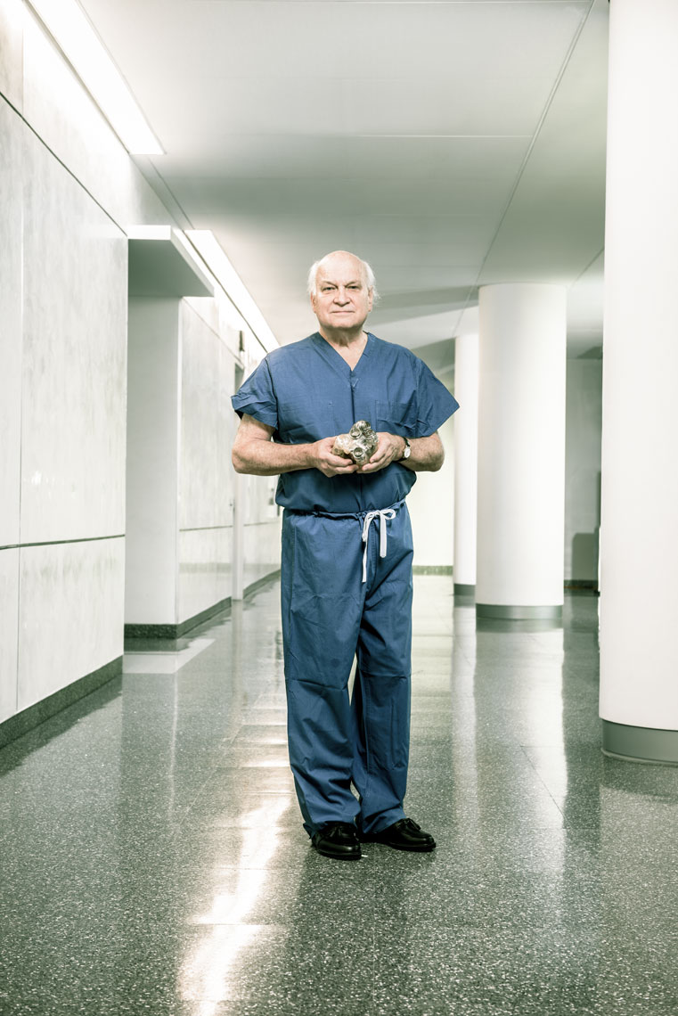 Dr. Duke Cameron holding an artificial heart and standing in a hallway in blue scrubs