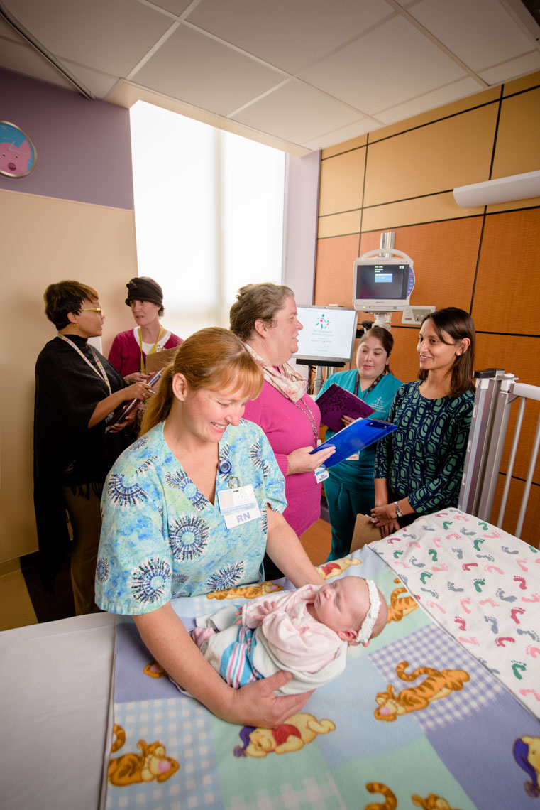 Dr. Monique Satput and pediatric experts stand in a patients room while a nurse holds a swaddled baby