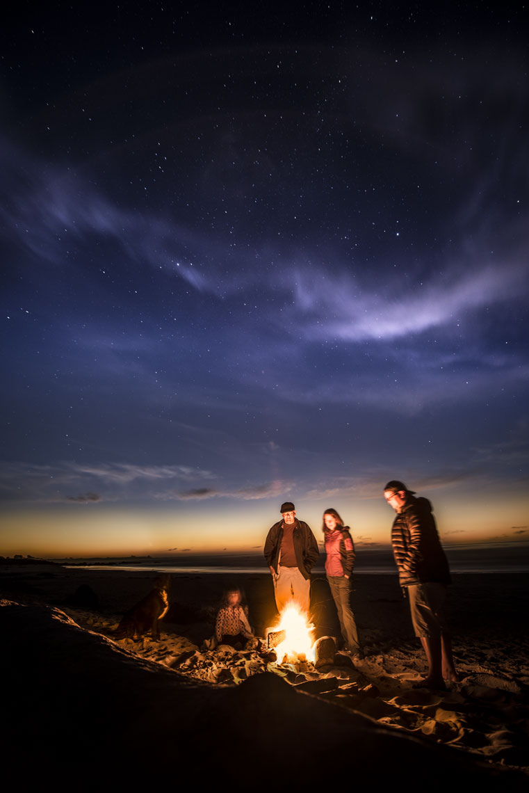 A family enjoys a fire on the beach under the night sky at Asilomar State Beach, Pacific Grove, California