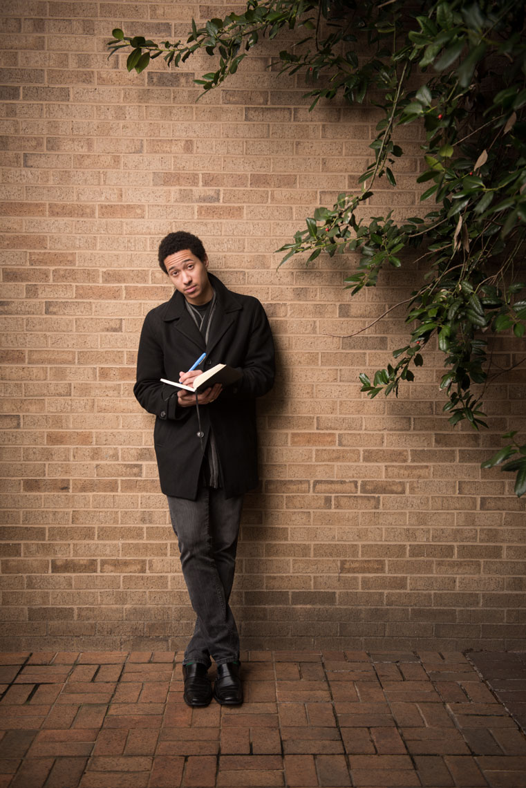 Youth Poet Laureate Derick Ebert looking up from a book and leaning against a wall