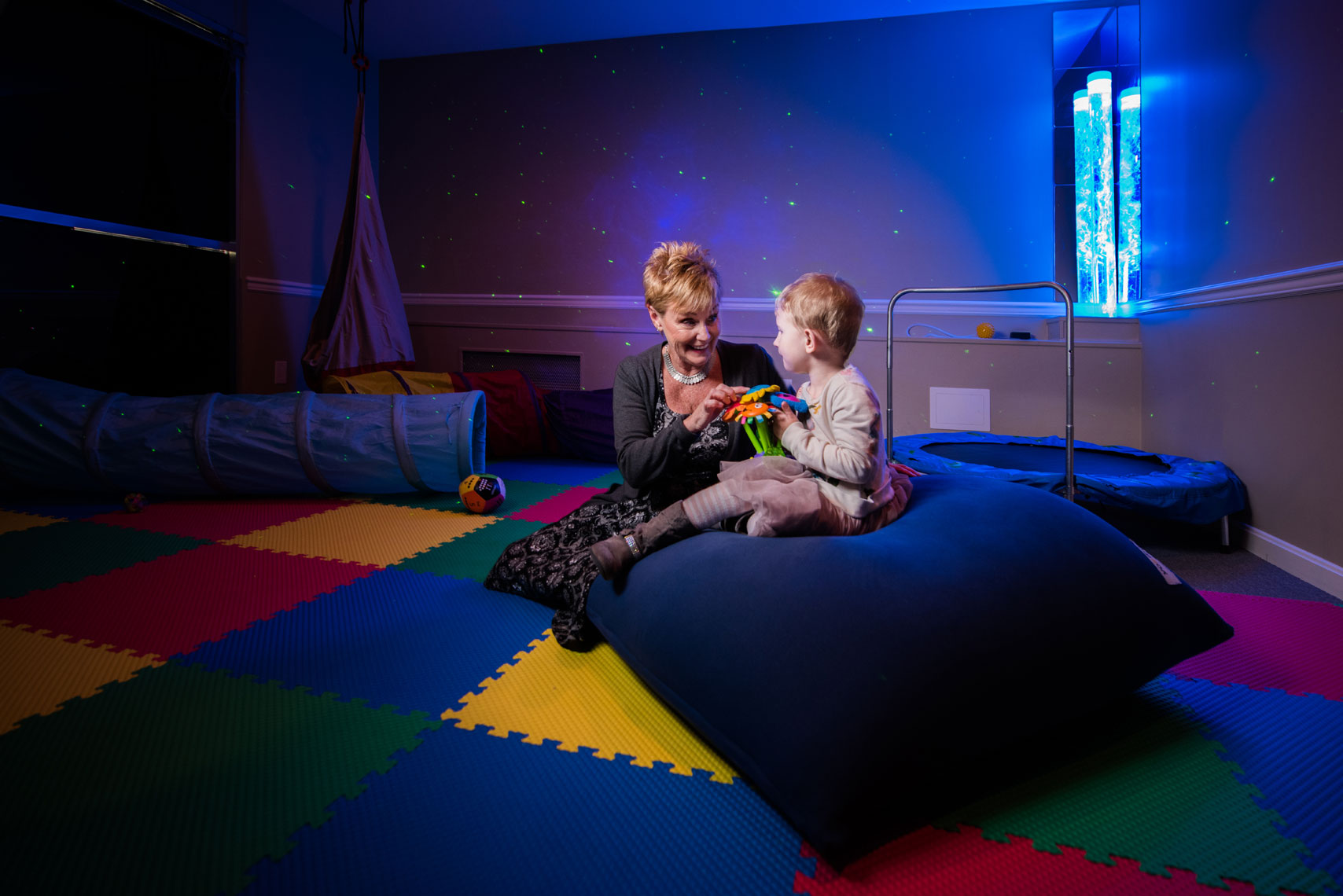 A teacher and a small child sit in a colorful sensory classroom