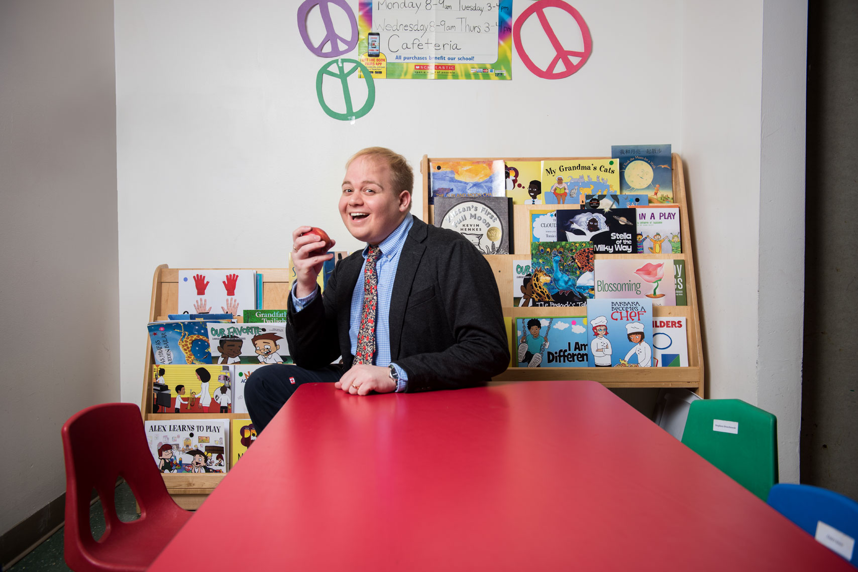 Principal Ryan Tauriainen sits at a kids school table smiling with an apple
