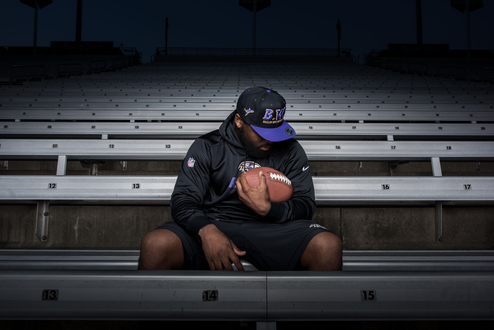 Football player sitting in empty stadium stands cradling a football