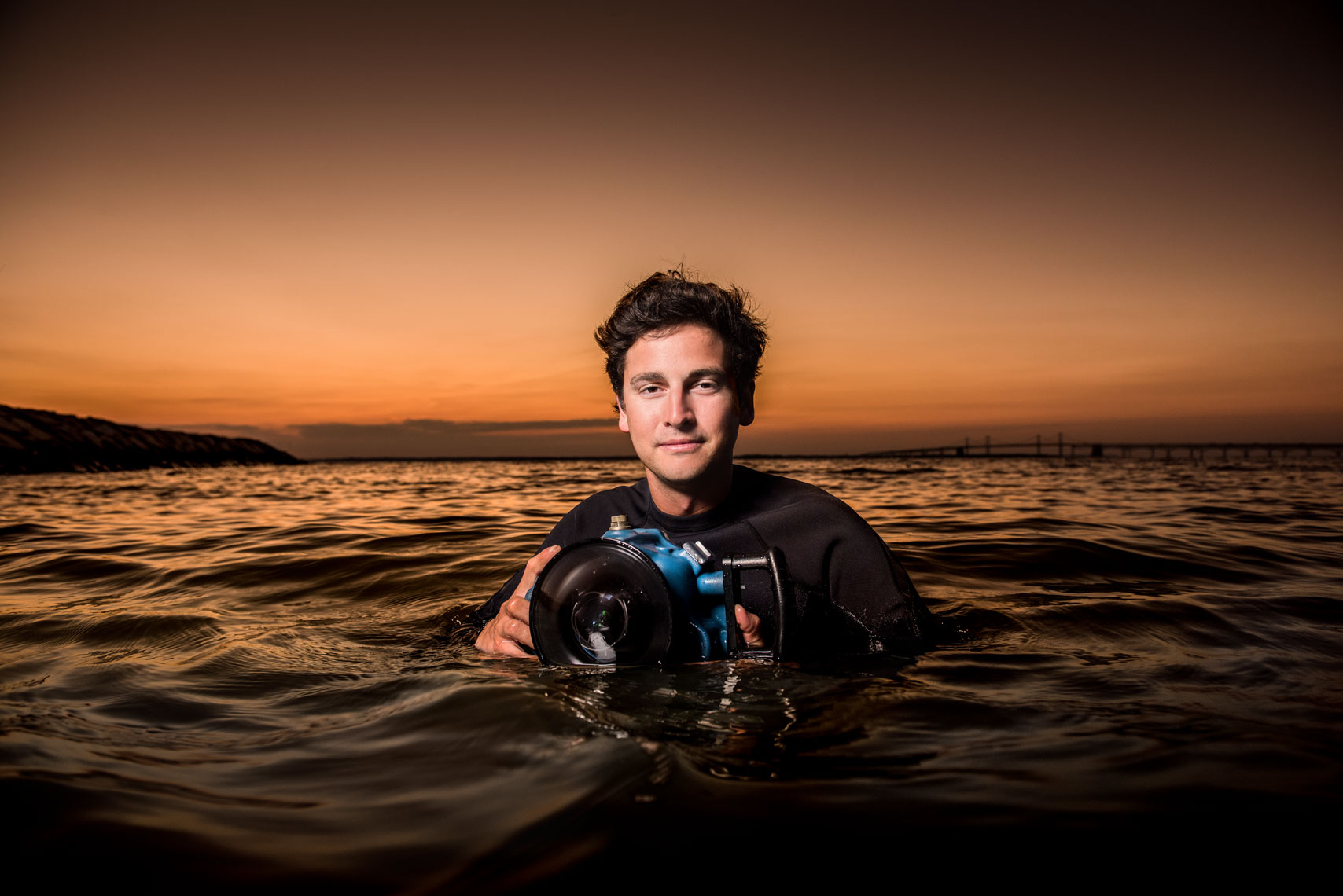 Jay P. Fleming holding an underwater camera while submerged in the Chesapeake Bay at sunset