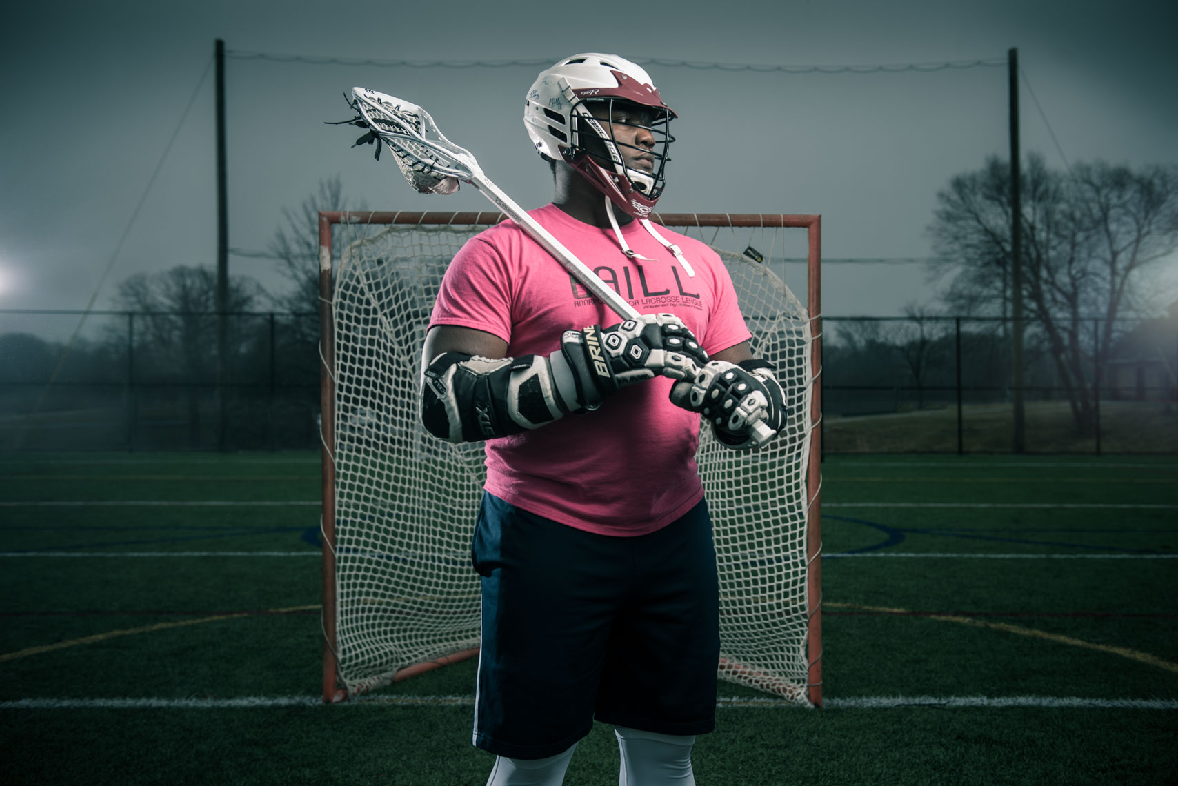Lacrosse player JoJo Bright holding a lacrosse stick in a pink shirt in front of a goal