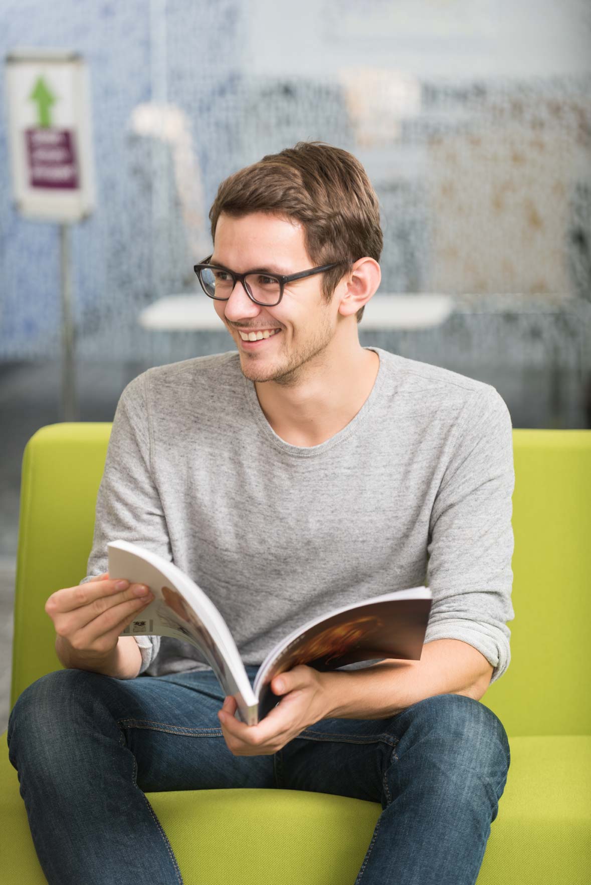 A student wearing glasses smiles while holding a magazine