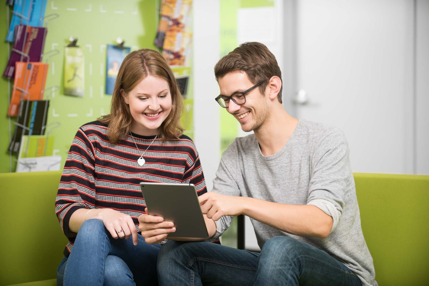 Two students smiling while holding a tablet device