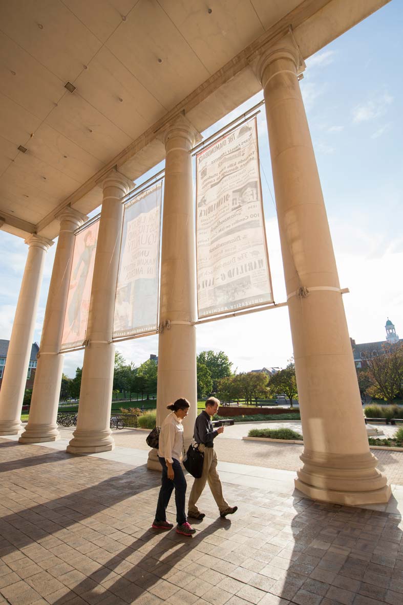 A student and a professor walk past columns on a college campus