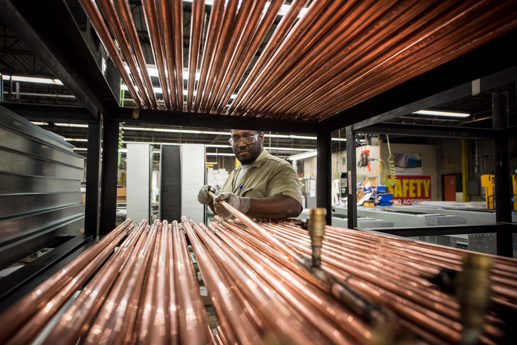 A factory worker places a piece of copper pipe on a shelf of copper pipes
