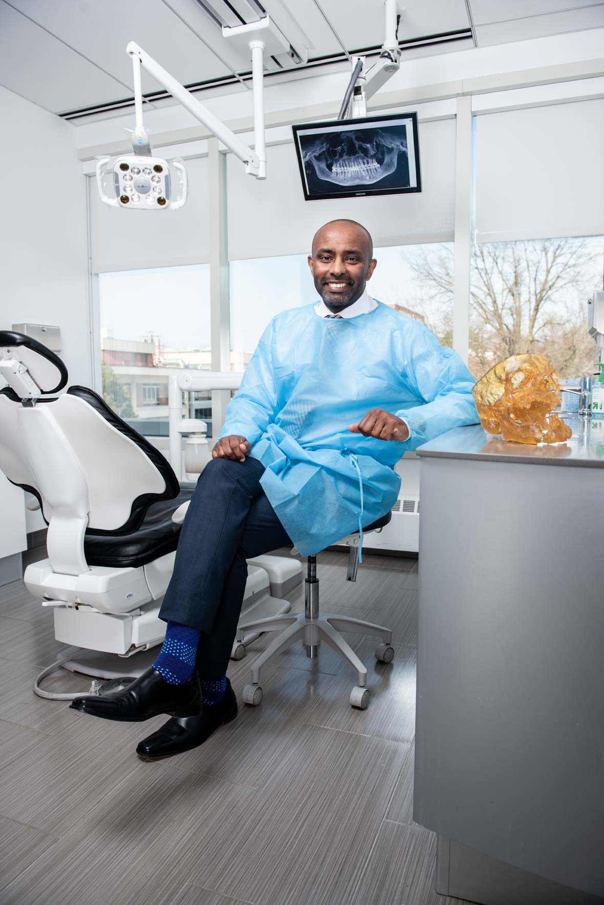 Dr. Ghassan Sinada wearing a smock and seated in front of a dental chair