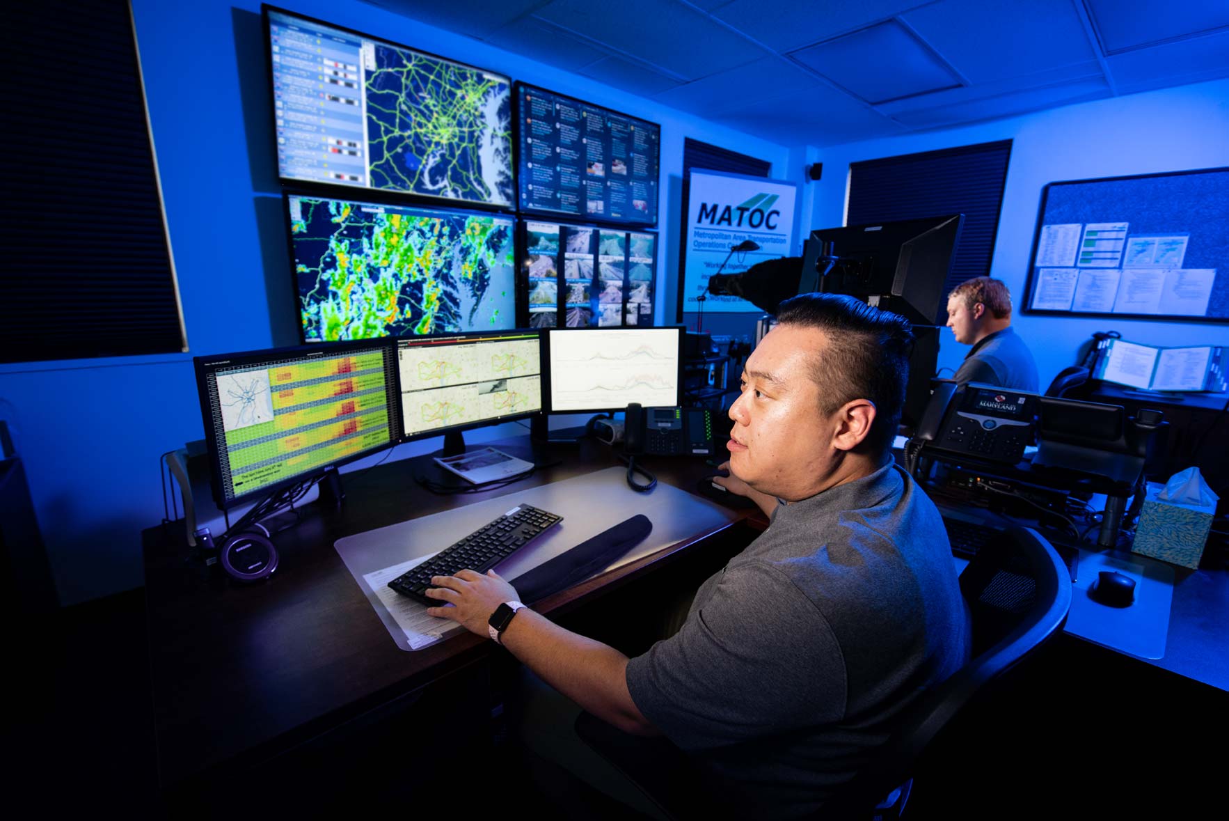 A man looks at computer screens in a blue room at the MATOC operations center