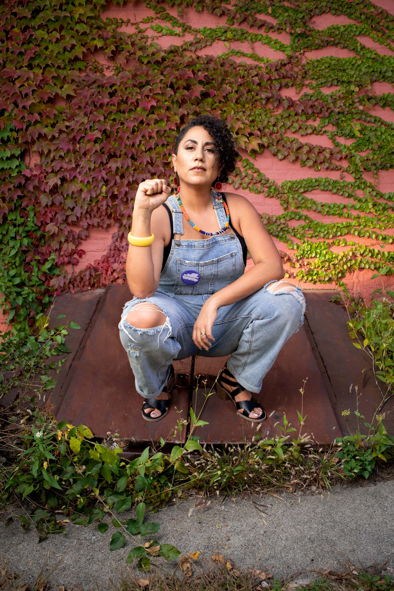 Taina Asili wearing overalls and crouching with a raised fist