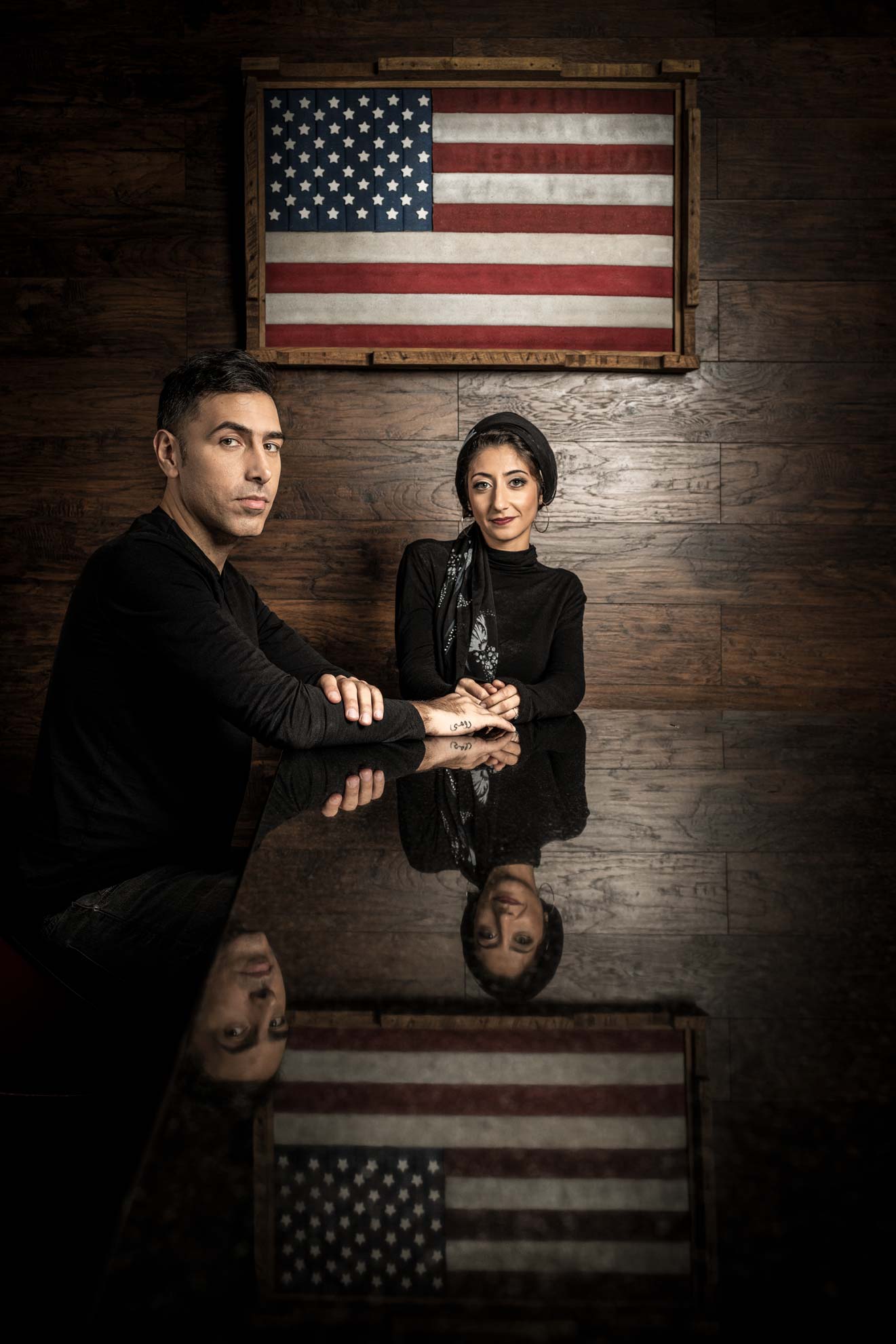 Rund Abdelfatah and Ramtin Arablouei seated at a bar top with the American flag reflected on the table