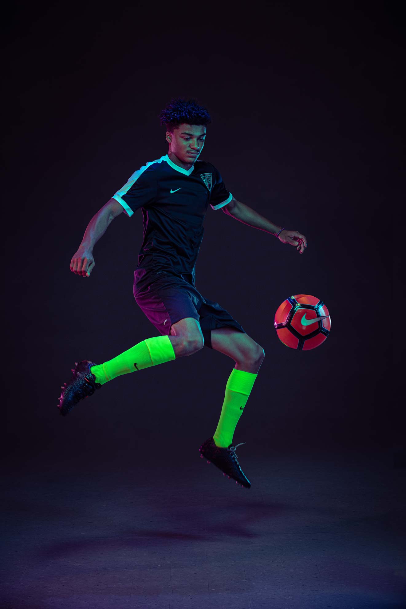 A soccer player jumping a kicking a ball in a studio environment