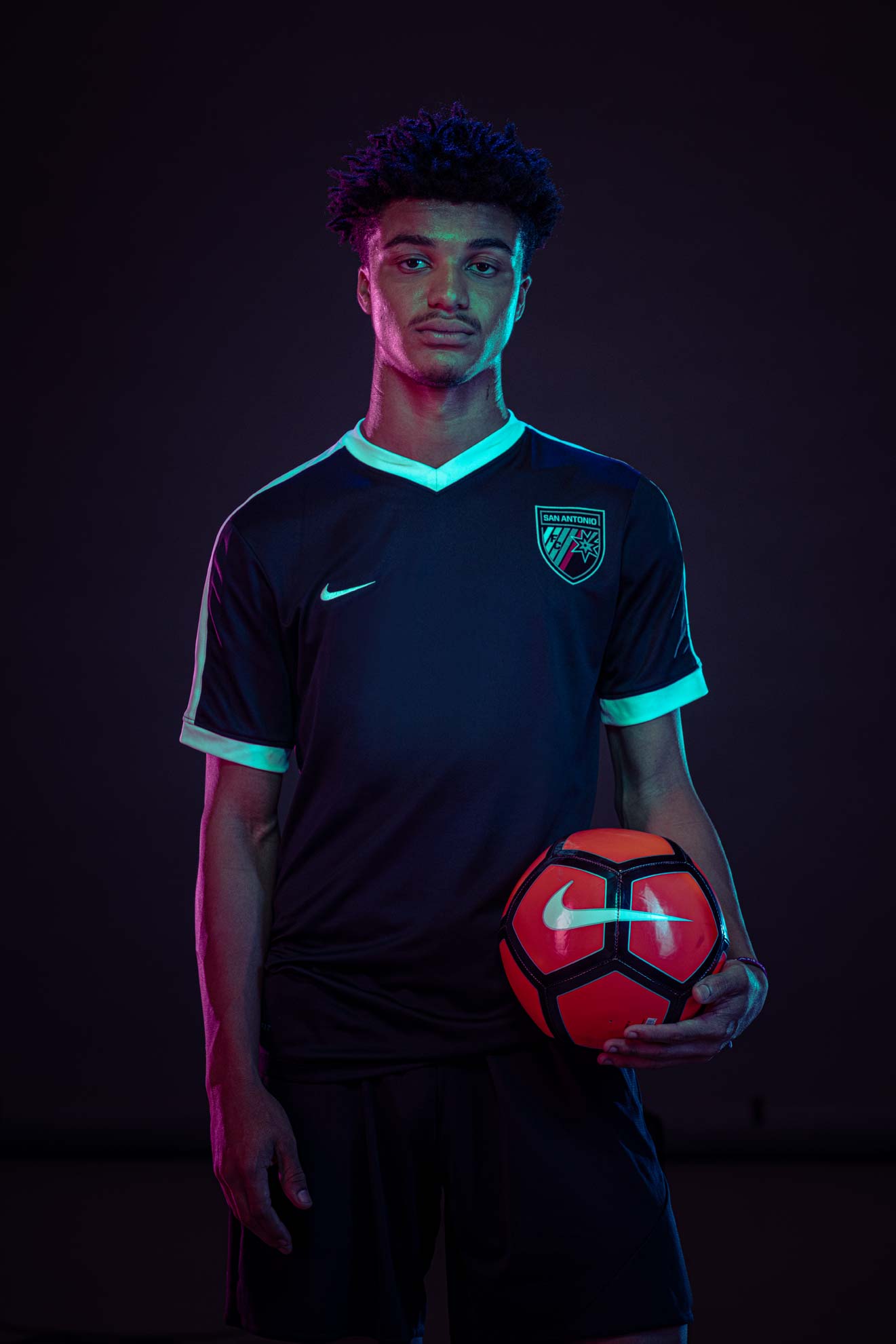 A soccer player standing and holding a Nike soccer ball in front of a dark background