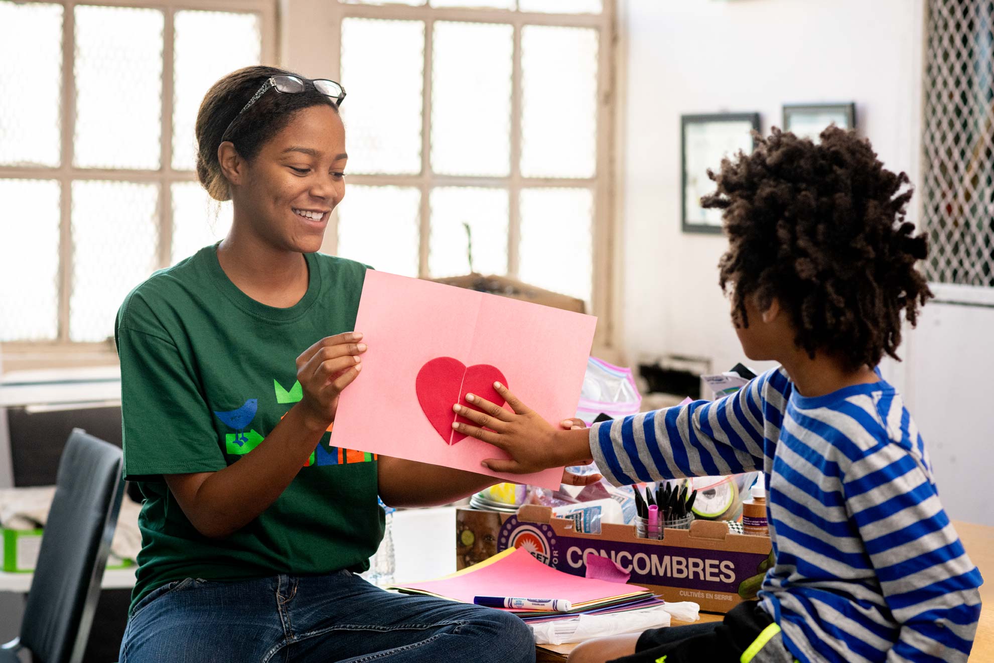 A teacher holds up a picture of a heart and a student reaches out and touches it