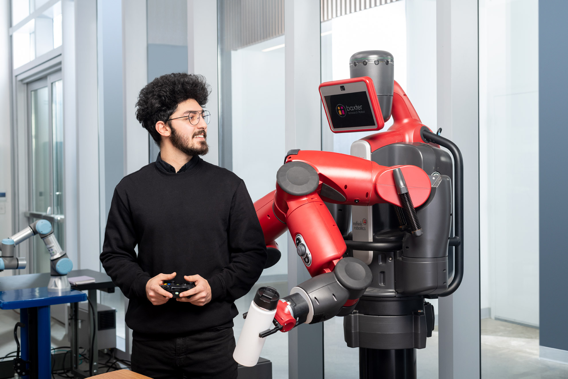 An engineering  student stands with Baxter the robot in a lab