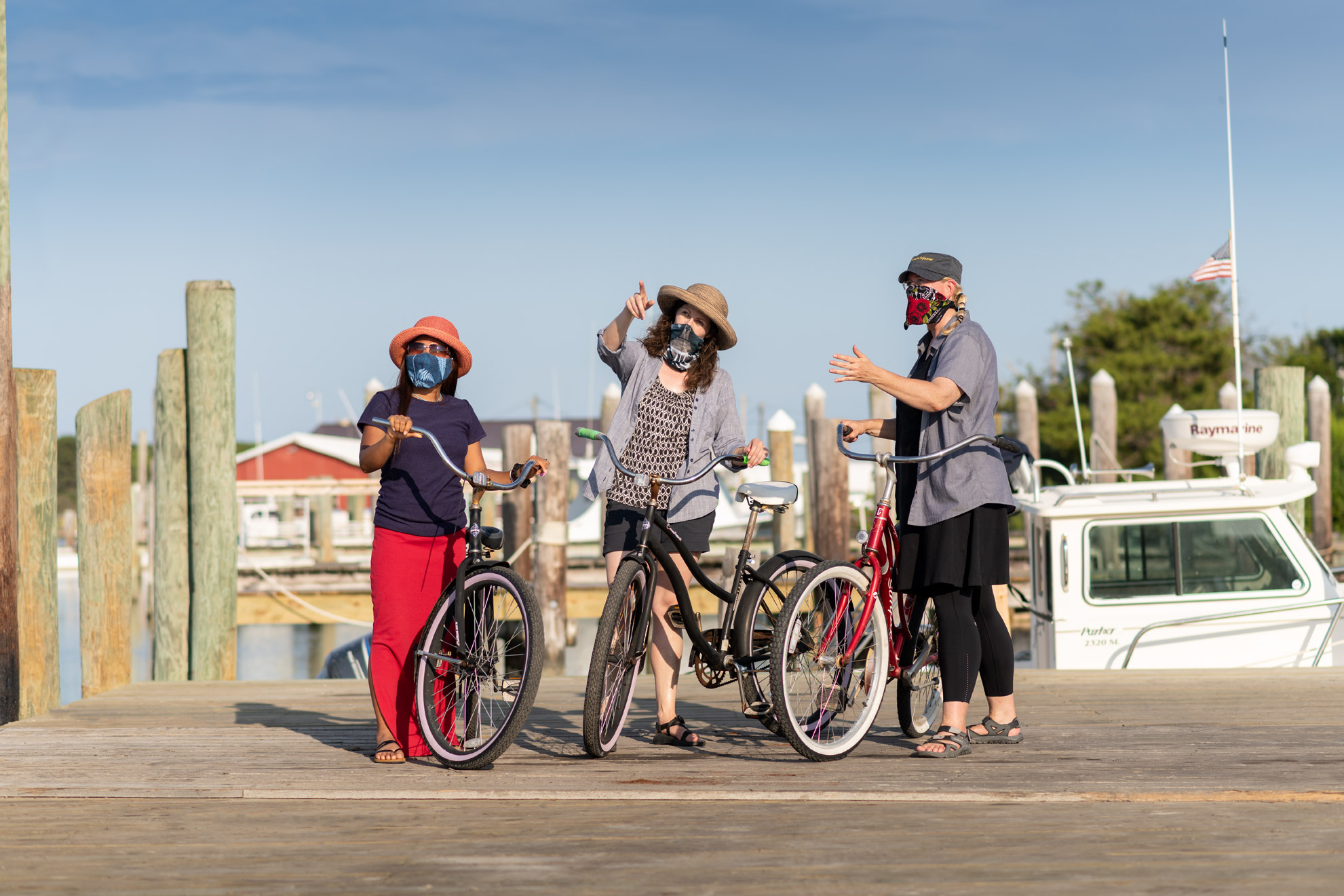 Three women with bicycles standing on a dock and pointing