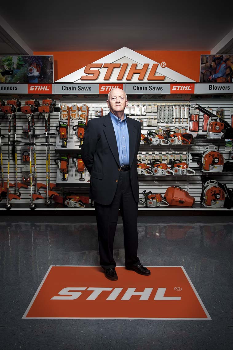 Stihl CEO Fred Whyte standing atop the company logo in front of a wall of Stihl products